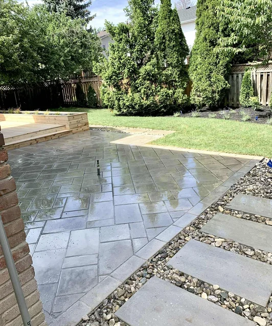 Interlock stone patio with herringbone pattern, river rock borders and raised cedar deck